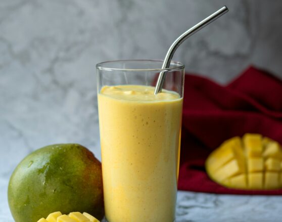 mango lassi smoothie in a glass with a straw and fresh mango next to it