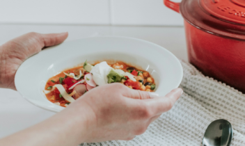 person holding a bowl of soup next to a stock pot
