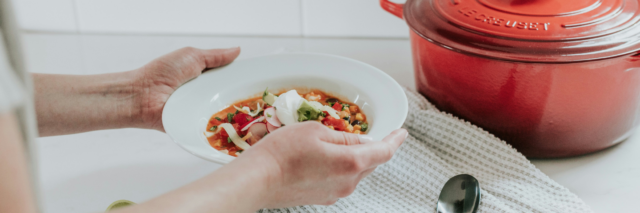 person holding a bowl of soup next to a stock pot