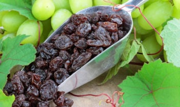 Spoon with raisins and green grapes in the background