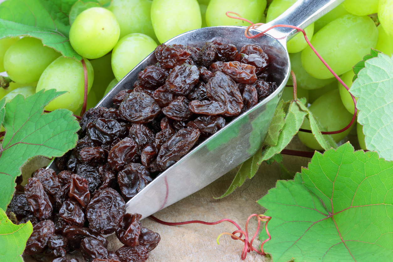 Spoon with raisins and green grapes in the background