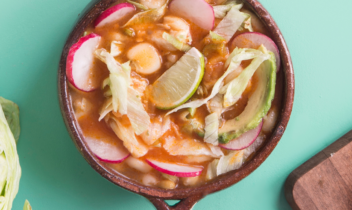 bowl of green chile posole with radish, lime, avocado on top
