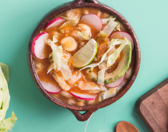 bowl of green chile posole with radish, lime, avocado on top