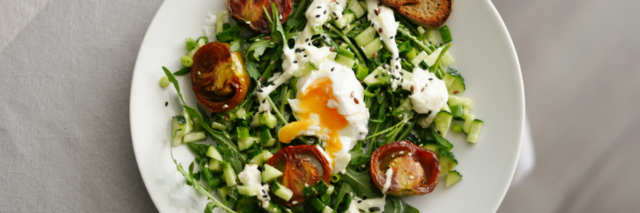 bowl of greens topped with a soft boiled egg and tomatoes