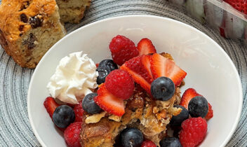 bowl of banana bread pudding topped with strawberries, blueberries and raspberries and a dollop of whipped cream
