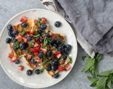 grilled halloumi cheese topped with strawberries blueberries and mint leaves