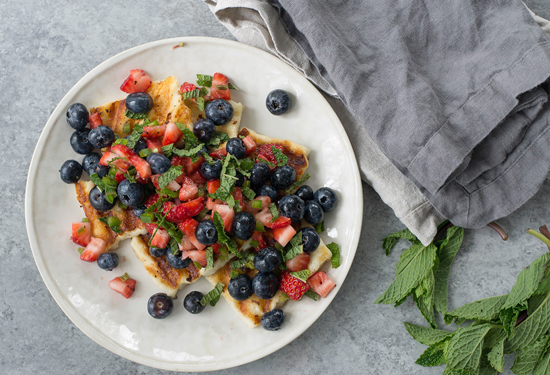 grilled halloumi cheese topped with strawberries blueberries and mint leaves