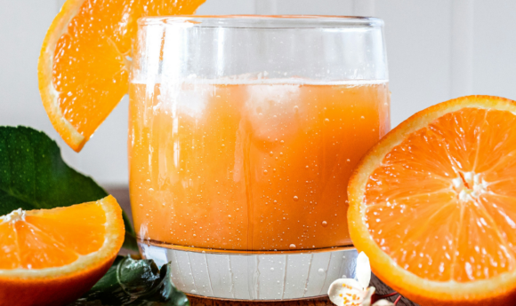 glass of fresh squeezed orange juice with fresh oranges next to it