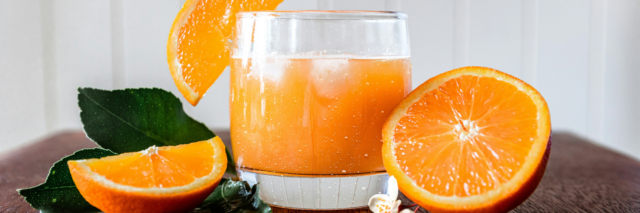 glass of fresh squeezed orange juice with fresh oranges next to it