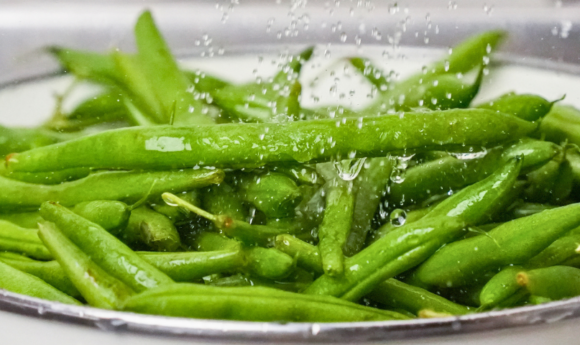 green beans in a colander with running water over them
