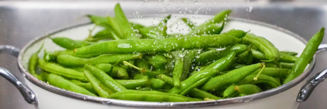 green beans in a colander with running water over them